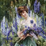 An image of a woman with brunette hair in an updo. She is wearing a pale green dress. She is holding freshly cut delphinium flowers, which are in shades of blue and purple. She is standing in front of a background of delphiniums and leaves. on September 27, 2024